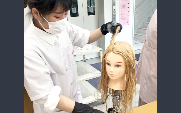 マネキンでヘアカラーの練習する学生
