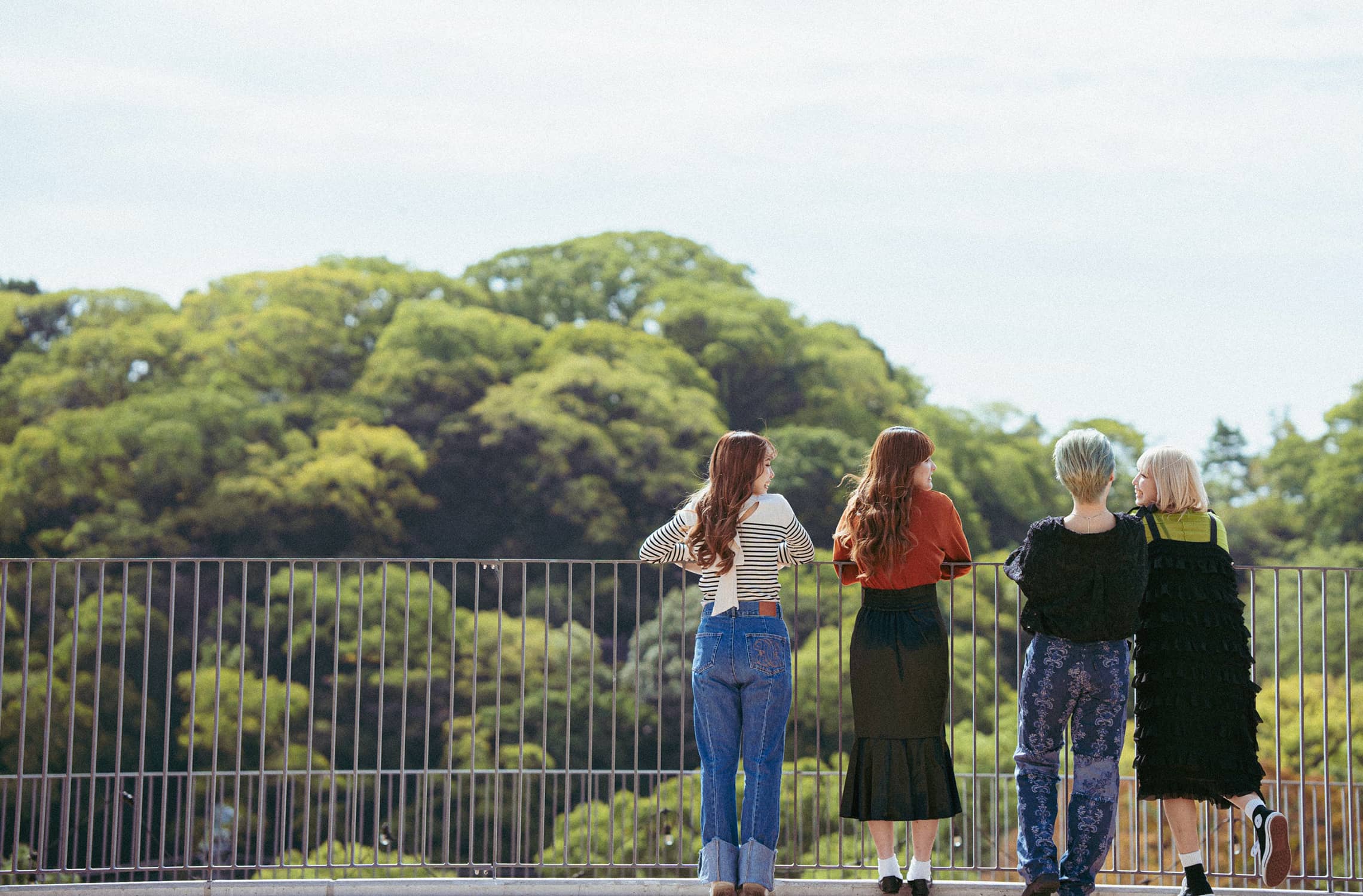 屋上の手すりの前に並んで緑の木々を見つめる女子学生達